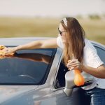 smiling young woman wiping automobile in countryside during car travel